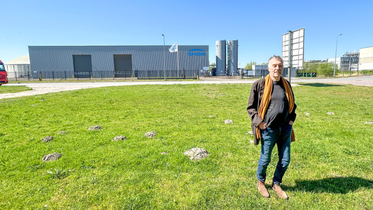 Man op een grasveld voor een industrieel gebouw met logo 'ENGIE', omringd door een hek met vlaggen.