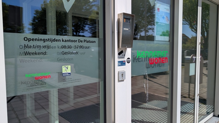 De ingang van het kantoor van Kennemer Wonen met openingstijden vermeld op de deur: maandag t/m vrijdag 08:30-17:00, weekend gesloten.