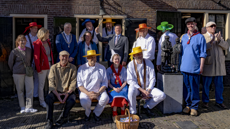Groep mensen in traditionele kaasdragerskleding poseert voor een historisch gebouw; sommige dragen kleurrijke hoeden.