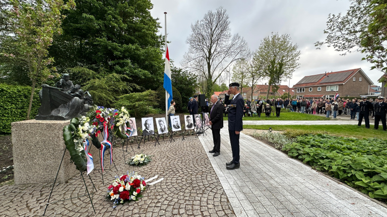 Mensen houden een herdenking bij een oorlogsmonument met vlag op halve mast en bloemstukken.