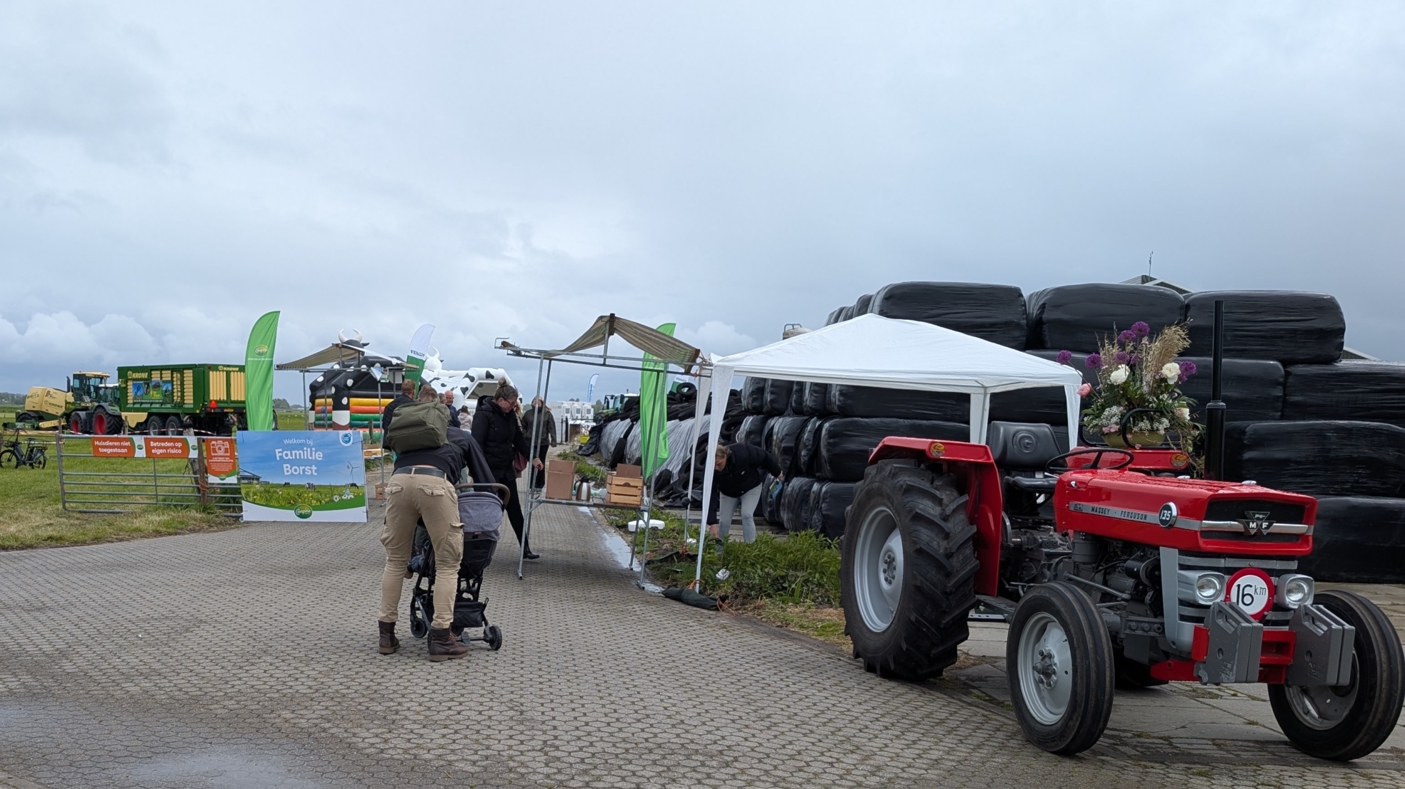Een man met een kinderwagen op een plattelandsweg, omringd door oude tractors en landbouwtentoonstellingen.