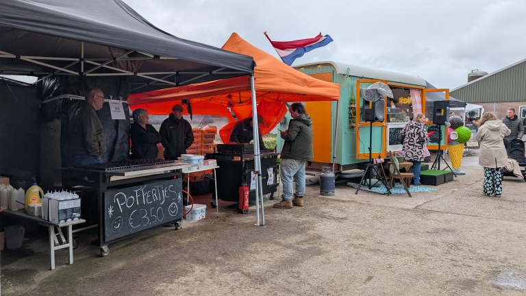 Straatvoedselmarkt met een kraam voor poffertjes en een oranje tent. Mensen staan bij een felgroene foodtruck.