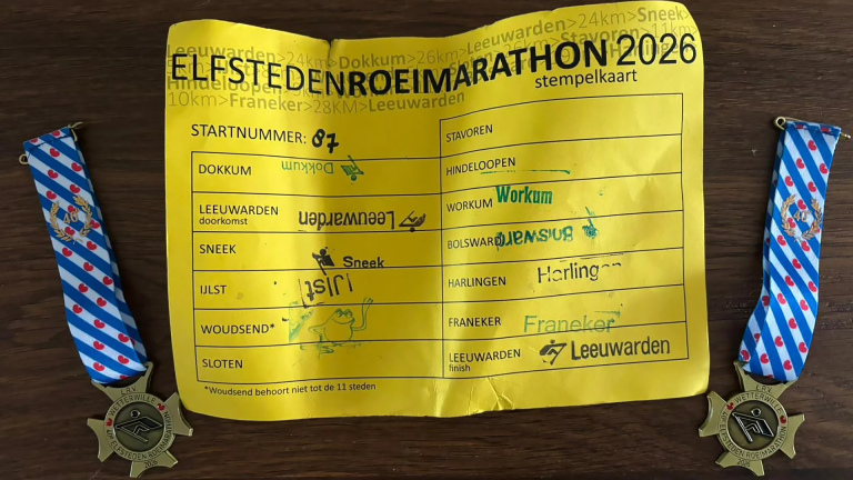 Een stempelkaart van de Elfstedentocht Roeimarathon 2026 met startnummer 87, geflankeerd door twee medailles met een blauw-wit lint.