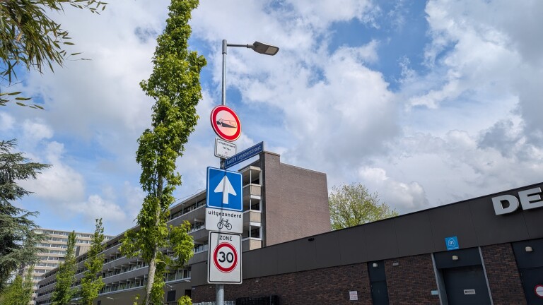 Verkeersborden bij Judith Leysterstraat waaronder eenrichtingsverkeer en 30 km/u zone, naast een groot gebouw en bomen.