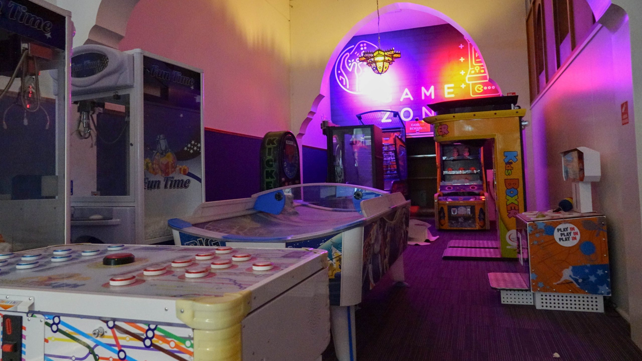 Binnenkant van een speelhal met diverse arcadekasten en opvallende neonverlichting.