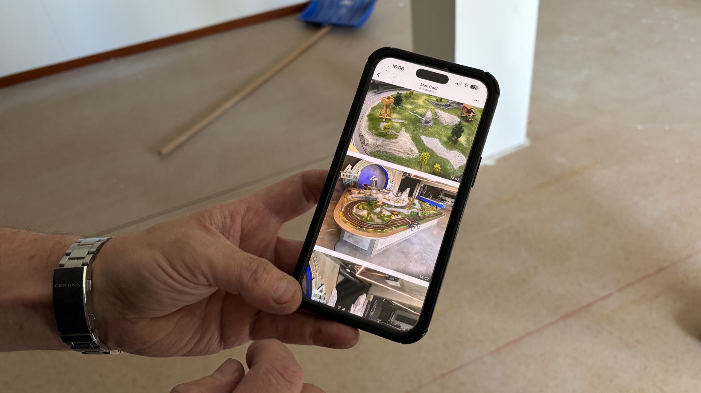 Persoon houdt een smartphone vast met daarop foto's van miniatuurlandschappen in een lege kamer.