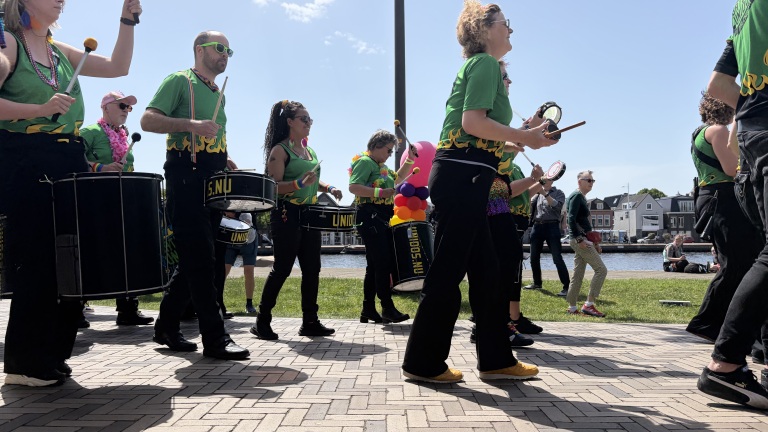 Een groep muzikanten in groene shirts speelt op trommels tijdens een evenement buiten bij zonnig weer.