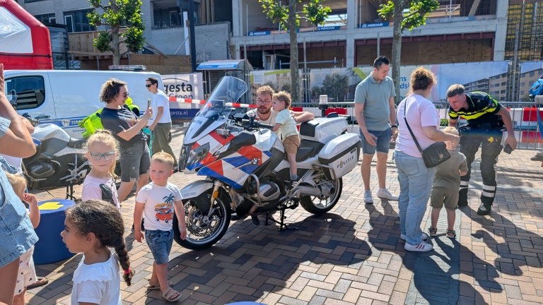 Kinderen bewonderen een politie-motorfiets op een plein, terwijl een agent met familieleden praat.