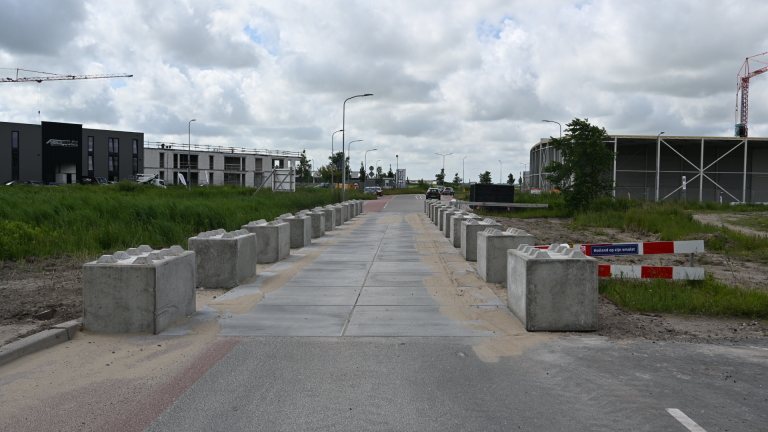 Betonnen blokken langs een smalle weg met aan weerszijden bouwterreinen en een bord met de tekst "Holland op z'n smalst".
