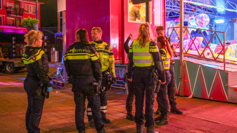 Agenten in uniform staan 's avonds samen voor een kleurrijke kermisattractie.