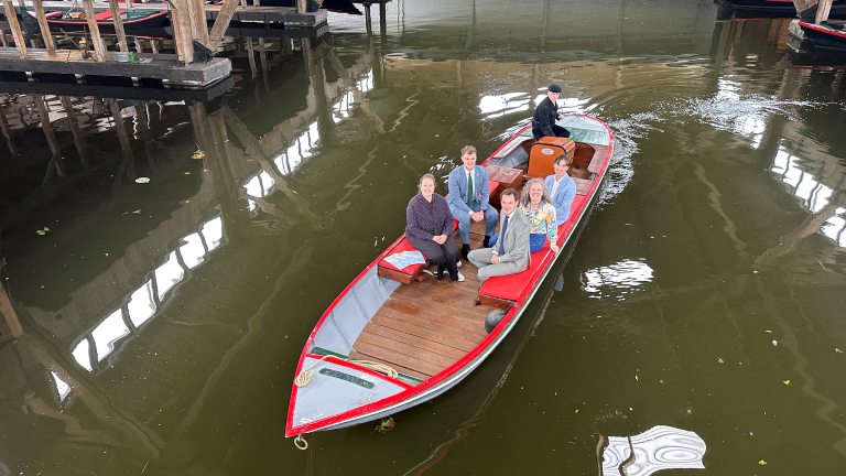 Mensen zitten in een rode boot in een overdekte waterlocatie, met een bestuurder aan de achterkant.