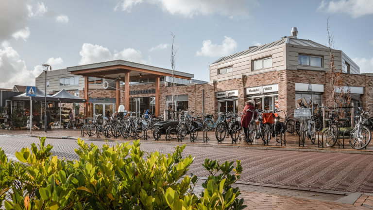 Winkelstraat met fietsenrekken en winkels, waaronder een viswinkel, op een zonnige dag met blauwe lucht.