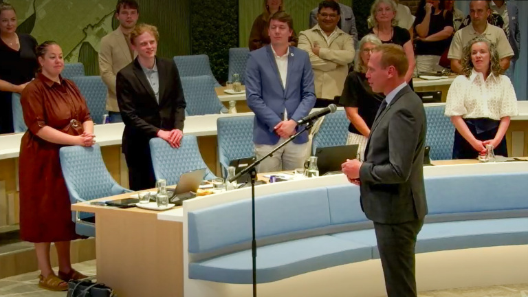 Een man in pak spreekt in een vergaderruimte voor een groep mensen die aandachtig luisteren.
