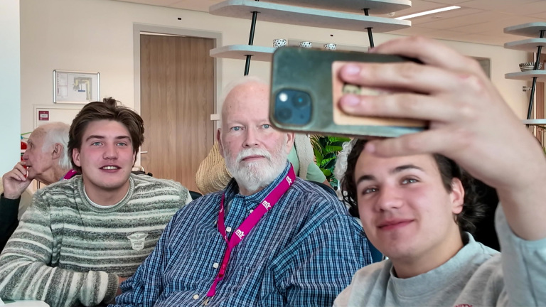 Twee jonge mannen en een oudere man maken een selfie in een binnenruimte.