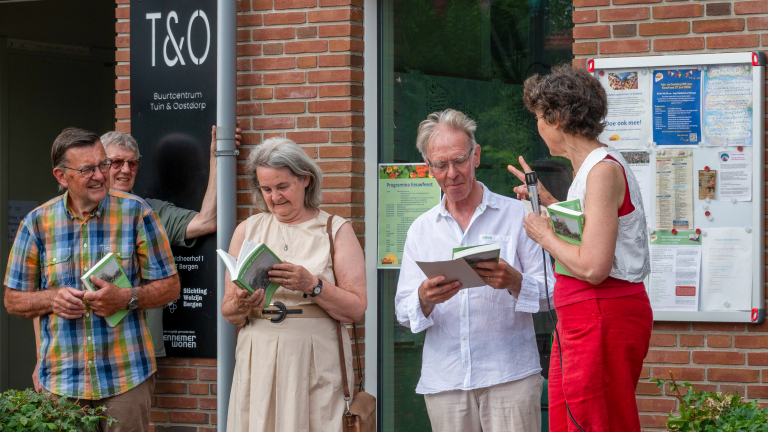 Een groep mensen staat voor een buurtcentrum met boeken in hun handen, in gesprek met elkaar.