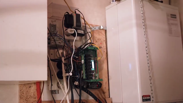 Elektrisch paneel met complexe bedrading naast een witte kast, verbonden met diverse kabels en stopcontacten.