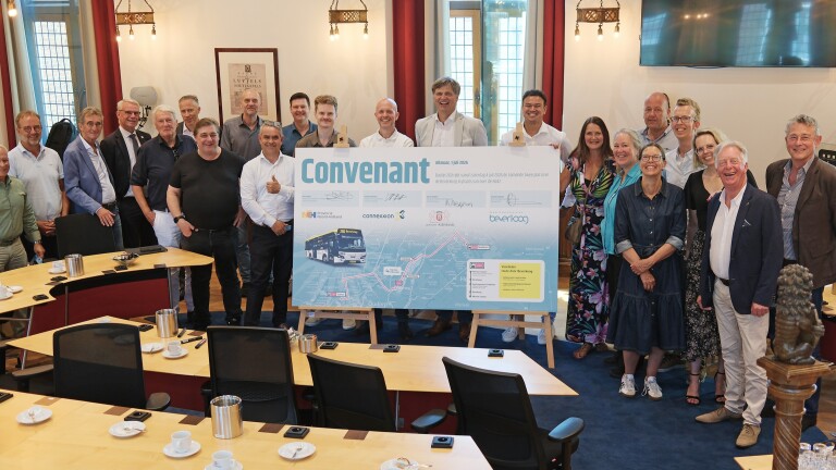 Groep mensen poseert met een groot bord waarop "Convenant" staat in een vergaderruimte met tafels en stoelen.