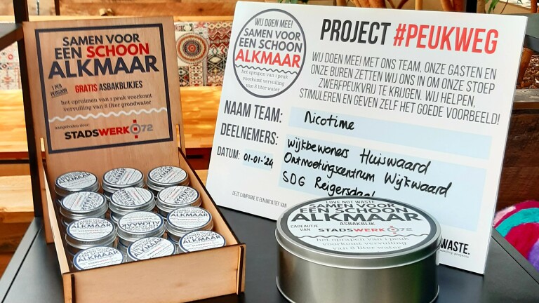 Borden en blikken promoten een schoonmaakactie in Alkmaar, met gratis asbakblikken van Stadswerk072 om vervuiling te verminderen.