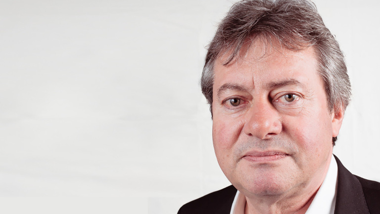 Close-up portret van een man met grijs haar in pak, tegen een lichte achtergrond