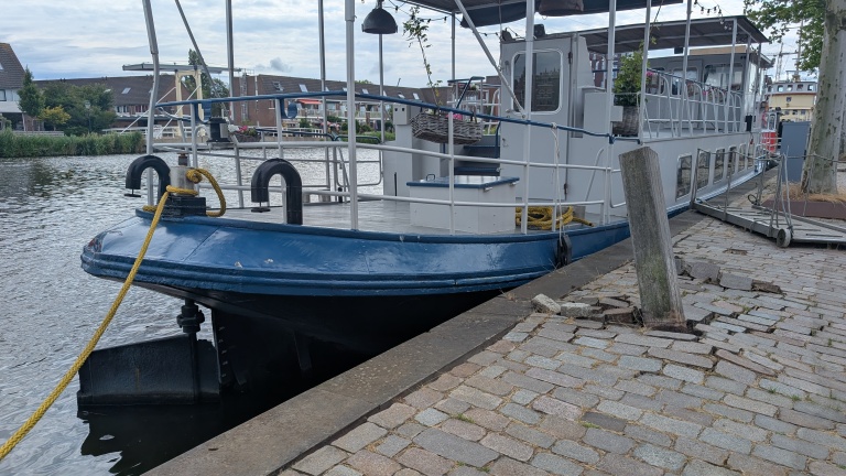 Een boot met een blauwe boeg ligt aangemeerd aan een kade met gebroken stenen.