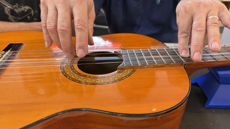 Close-up van handen die een klassieke gitaar bespelen, met vingers op de snaren bij het klankgat en de hals
