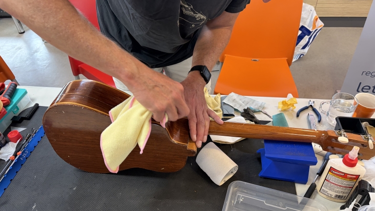 Iemand poetst de houten body van een klassieke gitaar op een werktafel met gereedschap en lijm