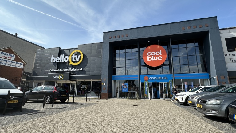 Gevel van winkels HelloTV en Coolblue met groot Coolblue-logo, seen vanaf parkeerplaats met geparkeerde auto’s
