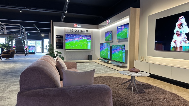 LG OLED-tv’s in een showroom met voetbal op de schermen, met een sofa en salontafel op de voorgrond