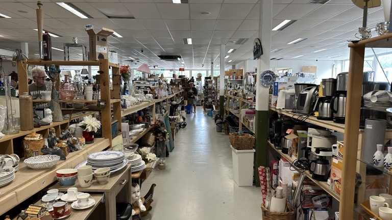 Gangpad in een kringloopwinkel met volle houten stellingen met servies, vazen, lampen en koffiezetapparaten