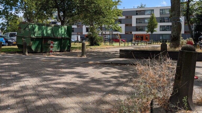 Groene bouwafvalcontainer in een woonwijk met bomen, speeltoestellen en flatgebouw op de achtergrond