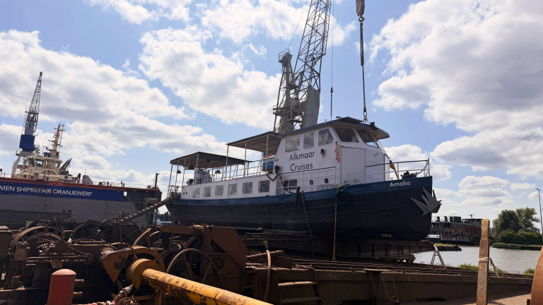 Rondvaartboot Amalia van Alkmaar Cruises op een werf, met hijskraan en groot schip op de achtergrond