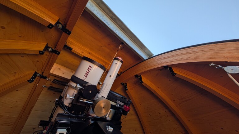 Telescoop gemonteerd in een houten sterrenwacht met open koepel en zicht op de blauwe lucht