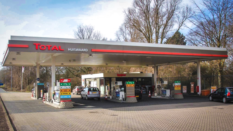 Total-tankstation Huiswaard met overkapping, benzinepompen en auto’s bij de pompen, met bomen op de achtergrond