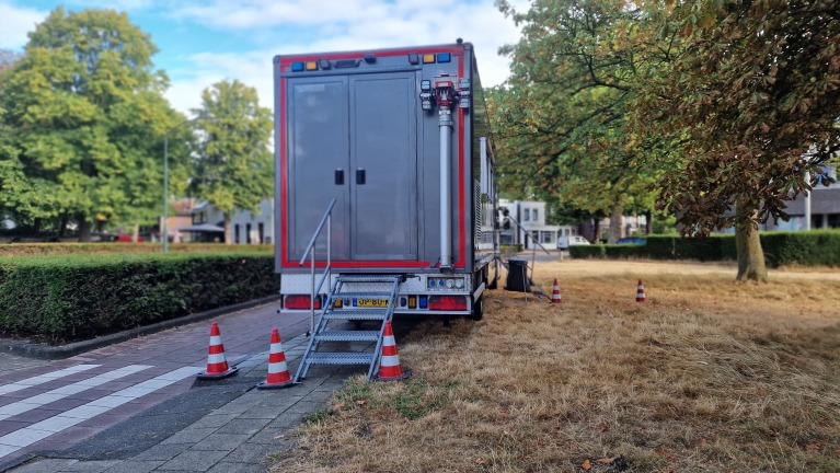 Achterkant van een geparkeerde brandweerwagen met trapje, afgezet met pionnen langs een parkachtig grasveld