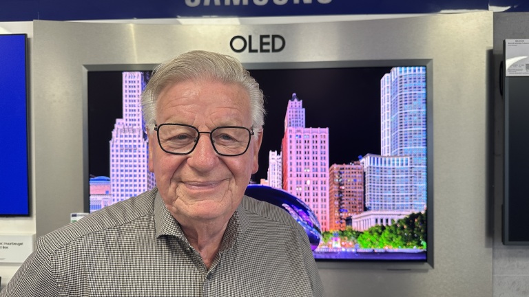 Oudere man met bril voor een OLED-tv in een winkel, met een kleurrijke stads skyline op het scherm
