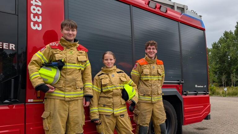 Drie brandweerlieden in bluspakken poseren met helmen voor een rode brandweerwagen met nummer 8333