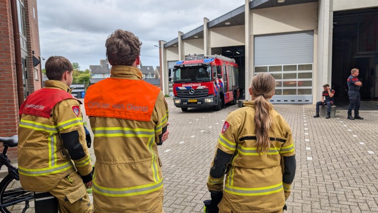 Brandweerlieden in uniform kijken naar een brandweerwagen die uit de kazerne rijdt