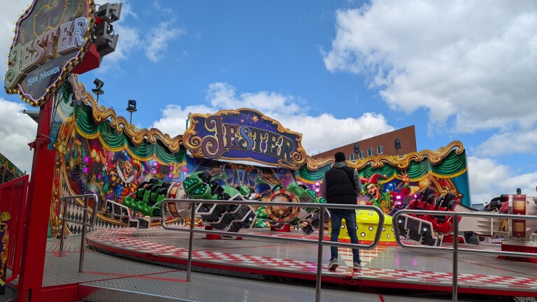 Kermisattractie met bord “Jester” en kleurrijke clownschilderingen, met draaiende gondels en een toeschouwer op het platform