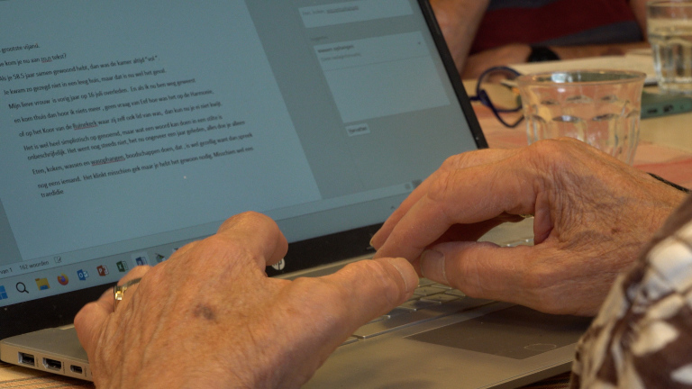 Handen typen op een laptop met een open tekstdocument, met een glas water op tafel op de achtergrond