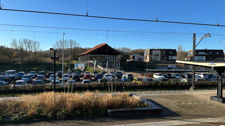 Parkeerterrein met auto’s voor het gebouw van archeologiemuseum Huis van Hilde, gezien vanaf een station perron