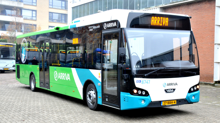 Groen-blauwe Arriva-stadsbus met display 'ARRIVA', geparkeerd bij gebouwen in de stad
