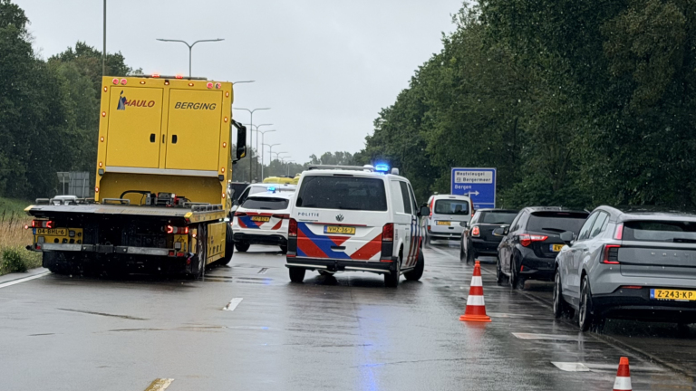 Politiebusjes en gele bergingswagen met zwaailichten op natte snelweg, met pionnen en langzaam rijdend verkeer