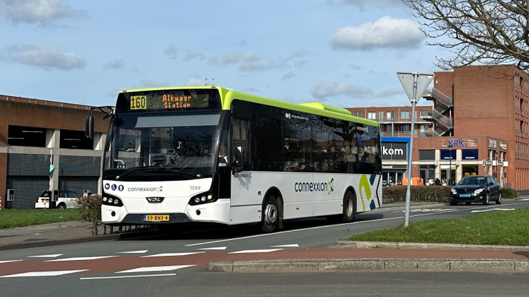 Witte Connexxion-bus op de weg met lijnnummer 160 en bestemming Alkmaar Station, met gebouwen op de achtergrond