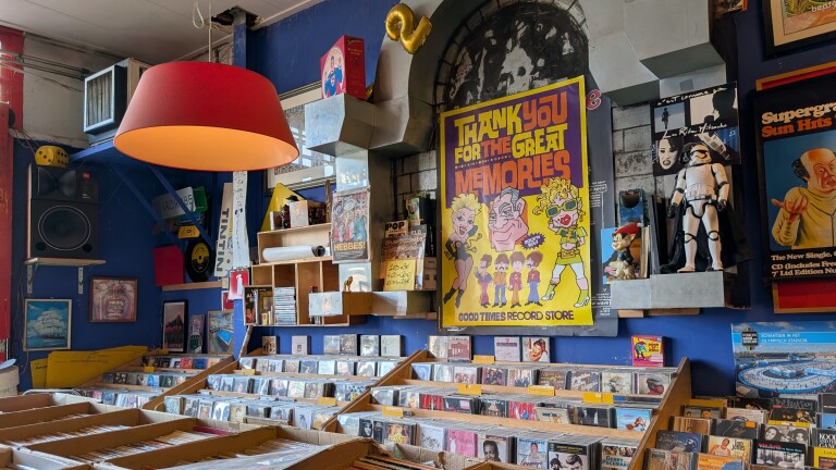 Interieur van een platenzaak met bakken vol cd’s, rode hanglamp en posters, waaronder “Thank you for the great memories”