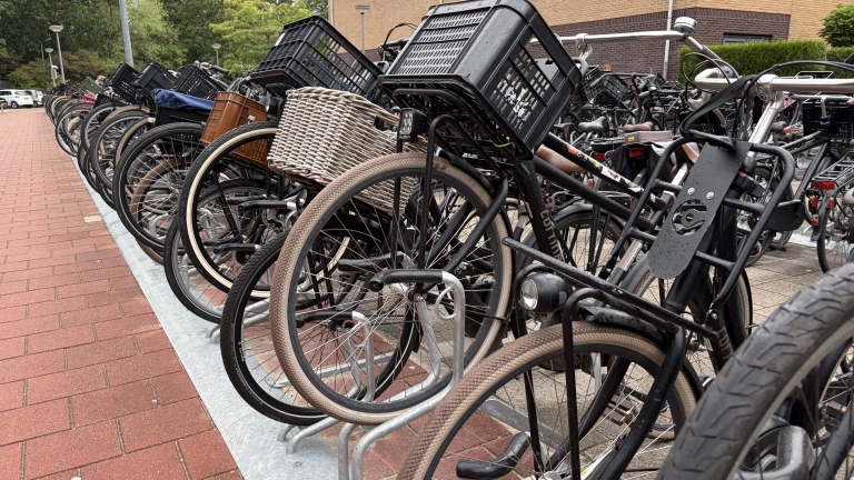 Rij geparkeerde fietsen met zwarte kratjes en een rieten mand in een fietsenrek bij een gebouw