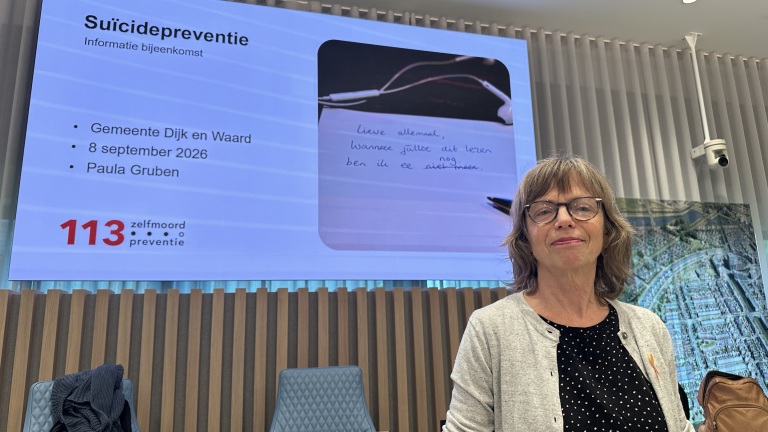 Vrouw voor presentatiescherm met slide Suïcidepreventie en 113 Zelfmoordpreventie, bij informatiebijeenkomst