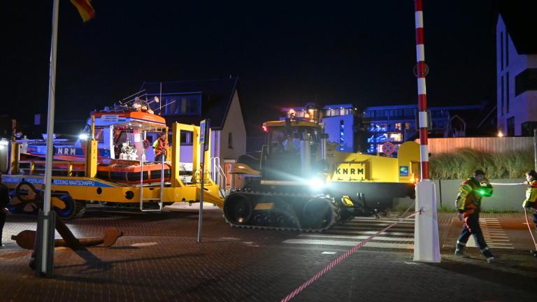 KNRM-reddingsboot op lanceerwagen wordt ’s nachts met werklichten verplaatst, met hulpverleners op de voorgrond