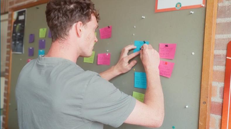 Man hangt kleurrijke post-its op een prikbord aan de muur