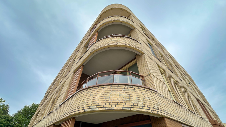 Laag standpunt van een hoekappartementencomplex met gele bakstenen en ronde balkons tegen een bewolkte lucht