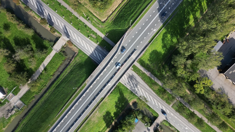 Luchtfoto van een kruispunt met een viaduct waar auto’s rijden, omringd door groen en een smal kanaal